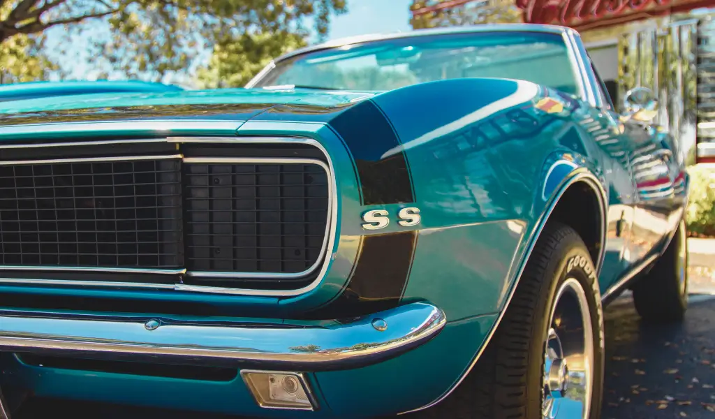 Klasyczny amerykański muscle car – dwudrzwiowe coupé z masywnym silnikiem V8 i agresywnym designem, zaparkowany na tle zachodzącego słońca.