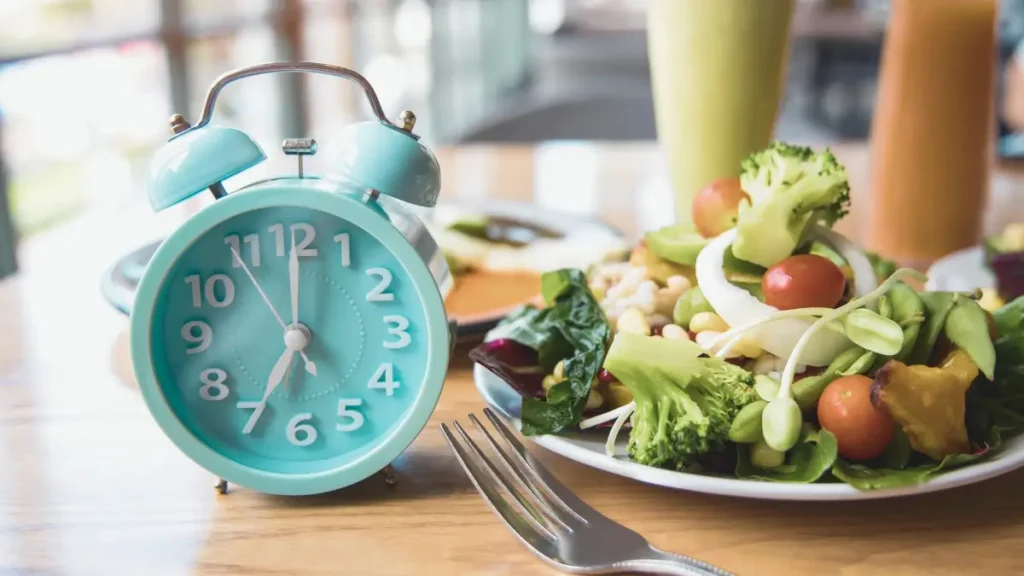 Zdrowy posiłek na talerzu obok zegara – symboliczne przedstawienie postu przerywanego (intermittent fasting) i okna żywieniowego 16/8