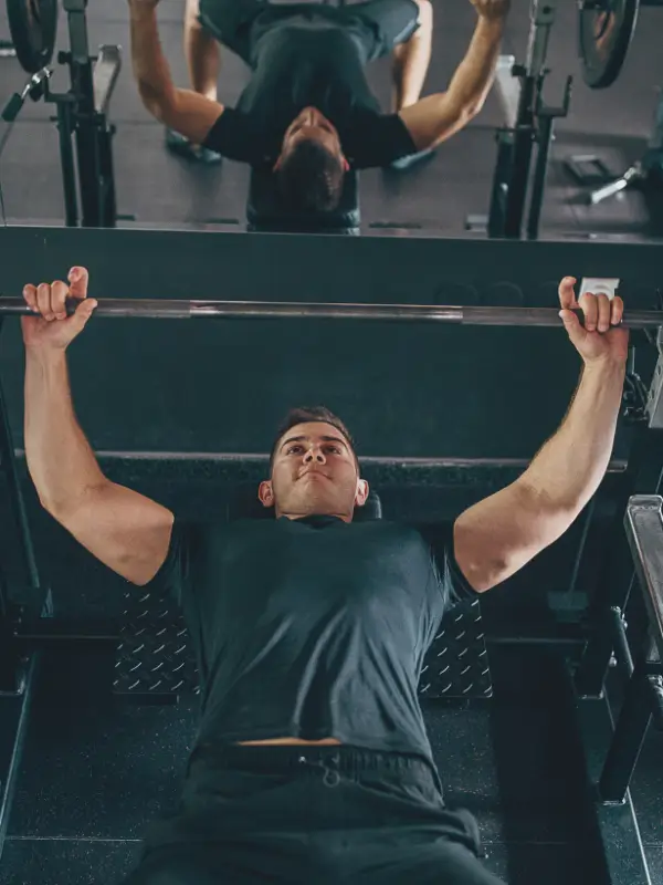 Mężczyzna wykonujący wyciskanie sztangi na ławce poziomej podczas treningu FBW na siłowni